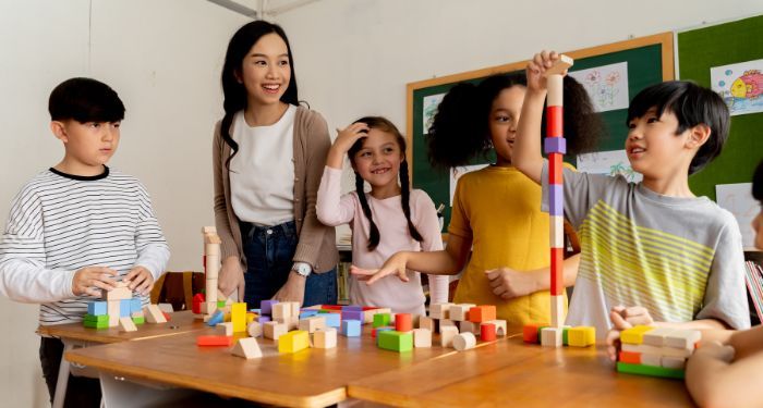 a teacher supervising four elementary school children playing with building blocks
